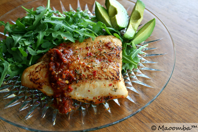 Orange poached catfish and avocado slices on a bed of arugula